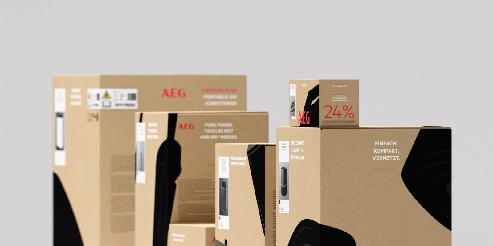 Multiple AEG product boxes of varying sizes arranged in a studio space on grey background, kraft cardboard with black product graphics and red wordmark