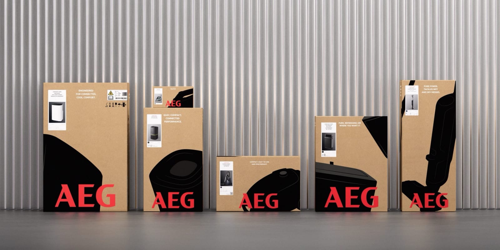 Five AEG product boxes in varying sizes lined up against corrugated metal wall, all kraft cardboard with black product silhouettes and red wordmark