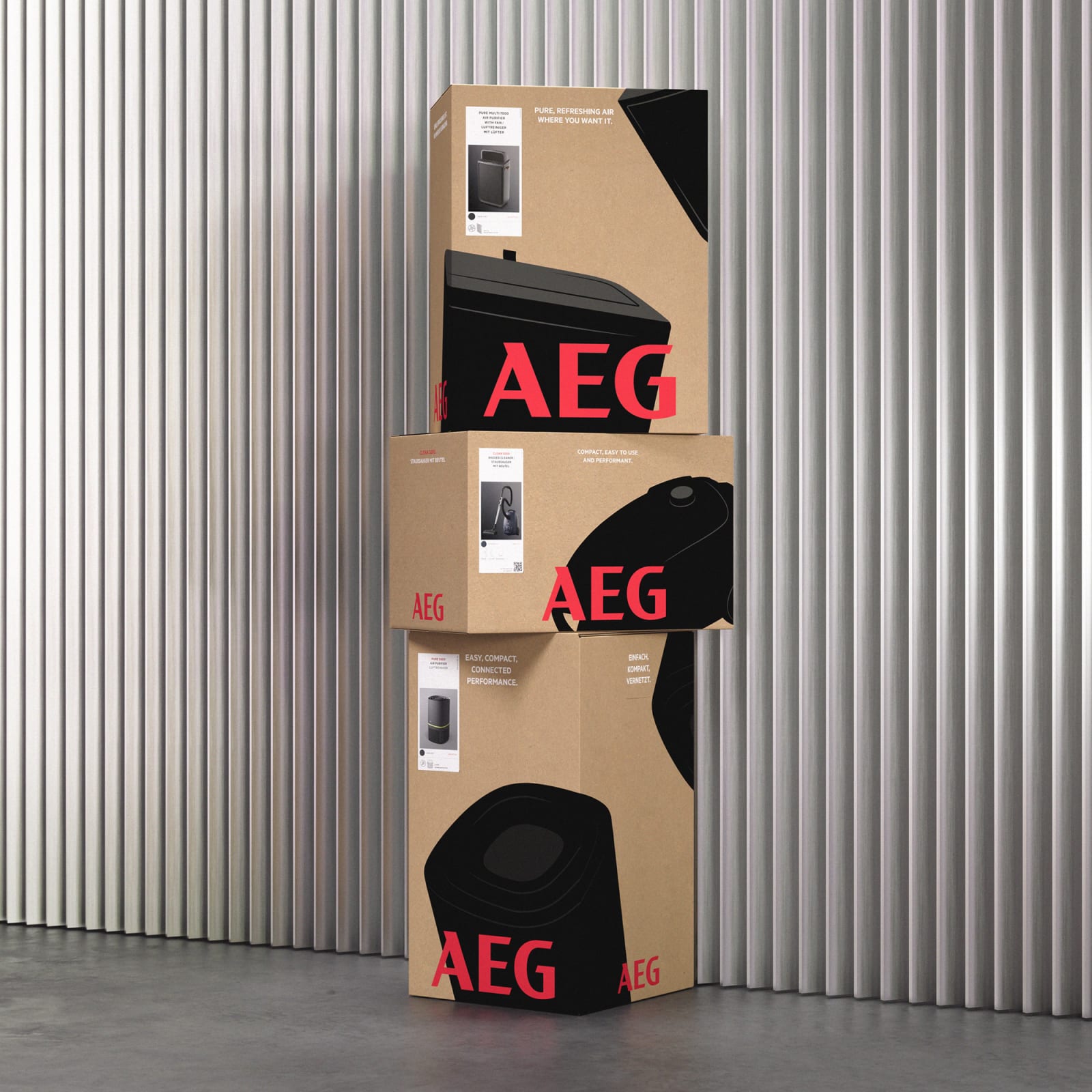 Three AEG product boxes stacked vertically against corrugated metal wall, kraft cardboard with bold black silhouettes and red AEG wordmark