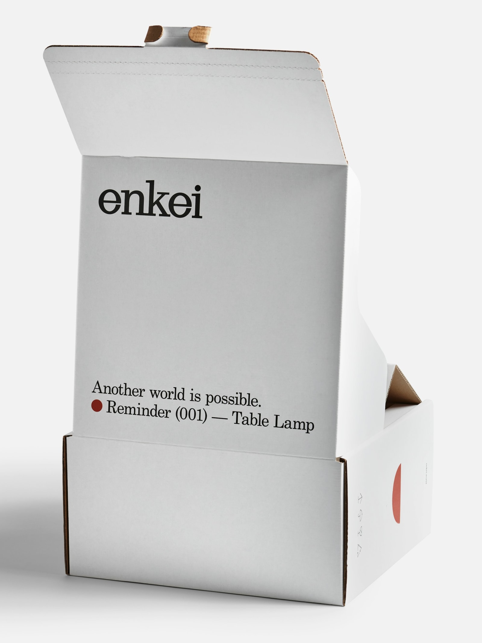 Enkei Reminder (001) Table Lamp white corrugated cardboard box partially opened showing interior with wordmark and product text on grey background