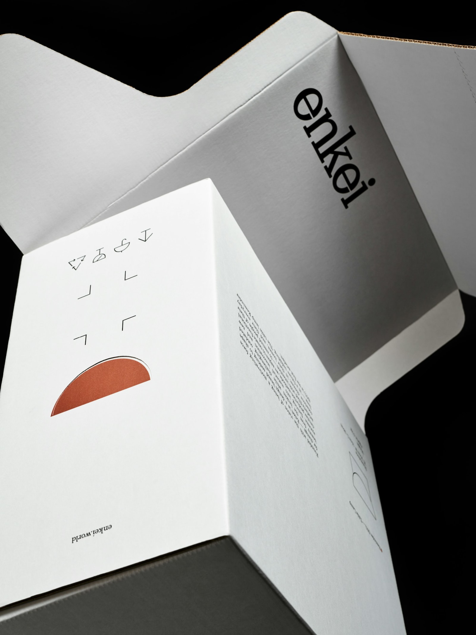 Enkei Reminder (001) Table Lamp box interior opened showing terracotta semicircle lamp graphic and assembly icons on both panels against black background