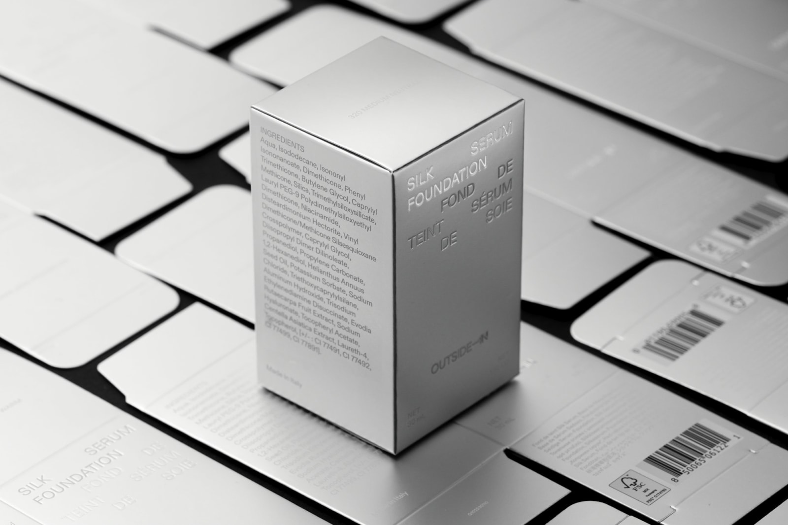 Outside-In Silk Foundation Serum metallic silver box resting on a grid of flat-packed dielines on grey background