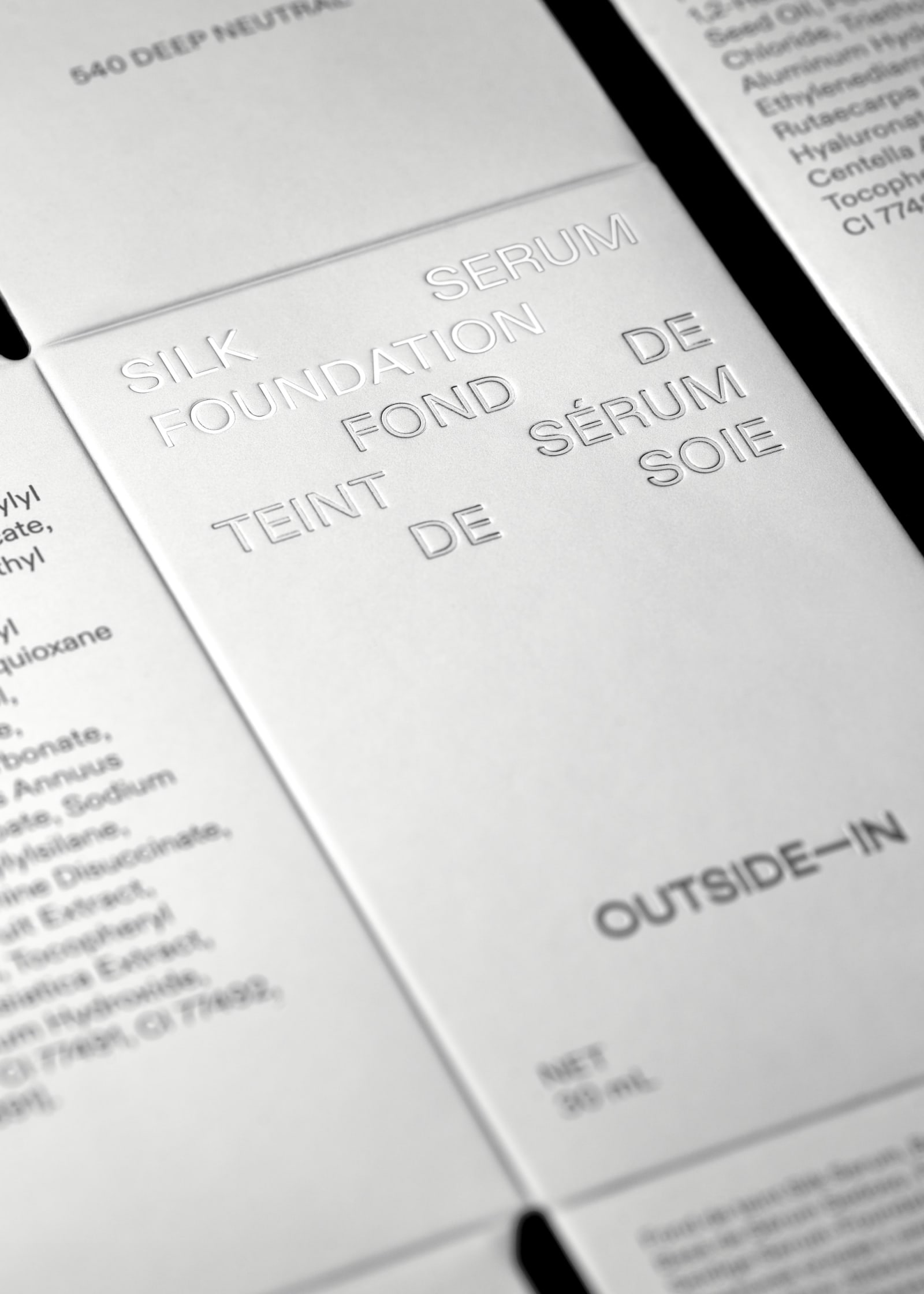 Close-up macro view of Outside-In Silk Foundation Serum metallic silver box face showing blind-embossed product name typography