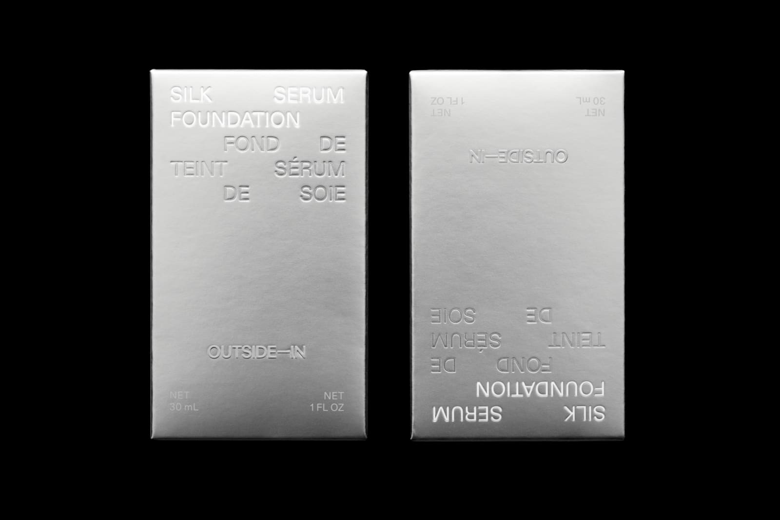 Two Outside-In Silk Foundation Serum metallic silver boxes on black background showing front face and mirrored back face
