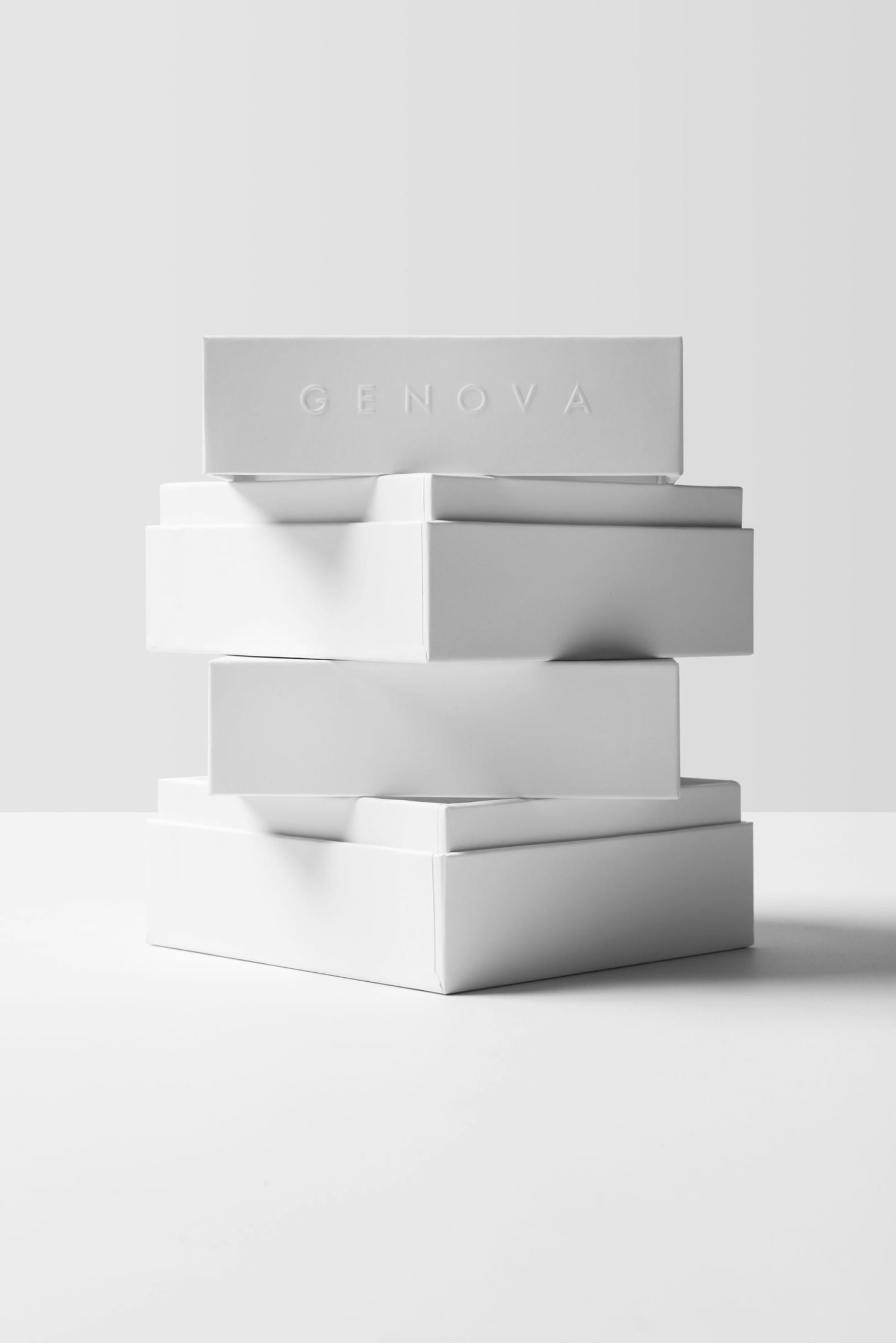 Four white rigid boxes stacked on top of each other with GENOVA blind-embossed on the top box side face against grey background