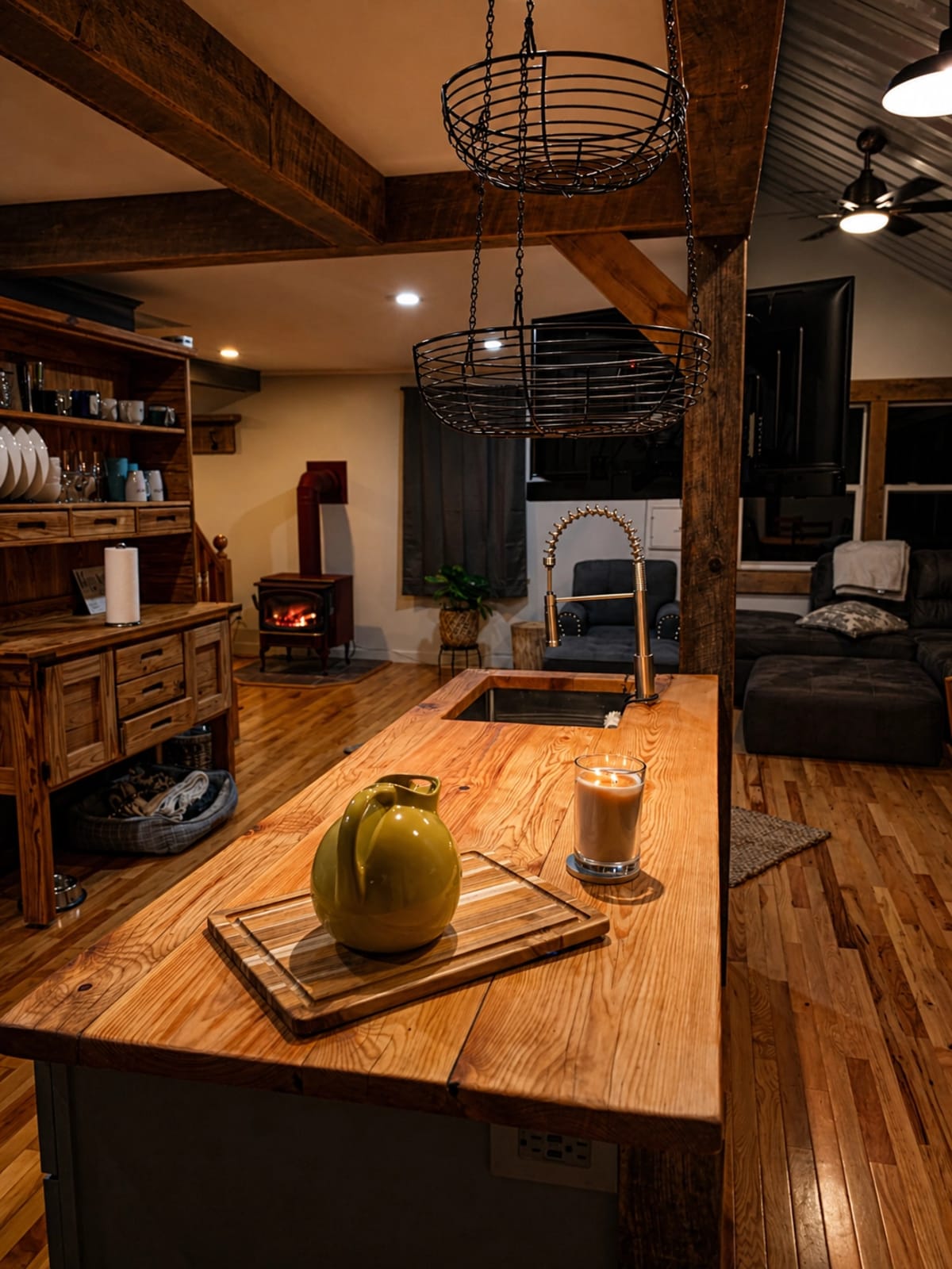 Wood countertop island with black sink, hanging wire baskets, rough-sawn beam, and warm cabin lighting