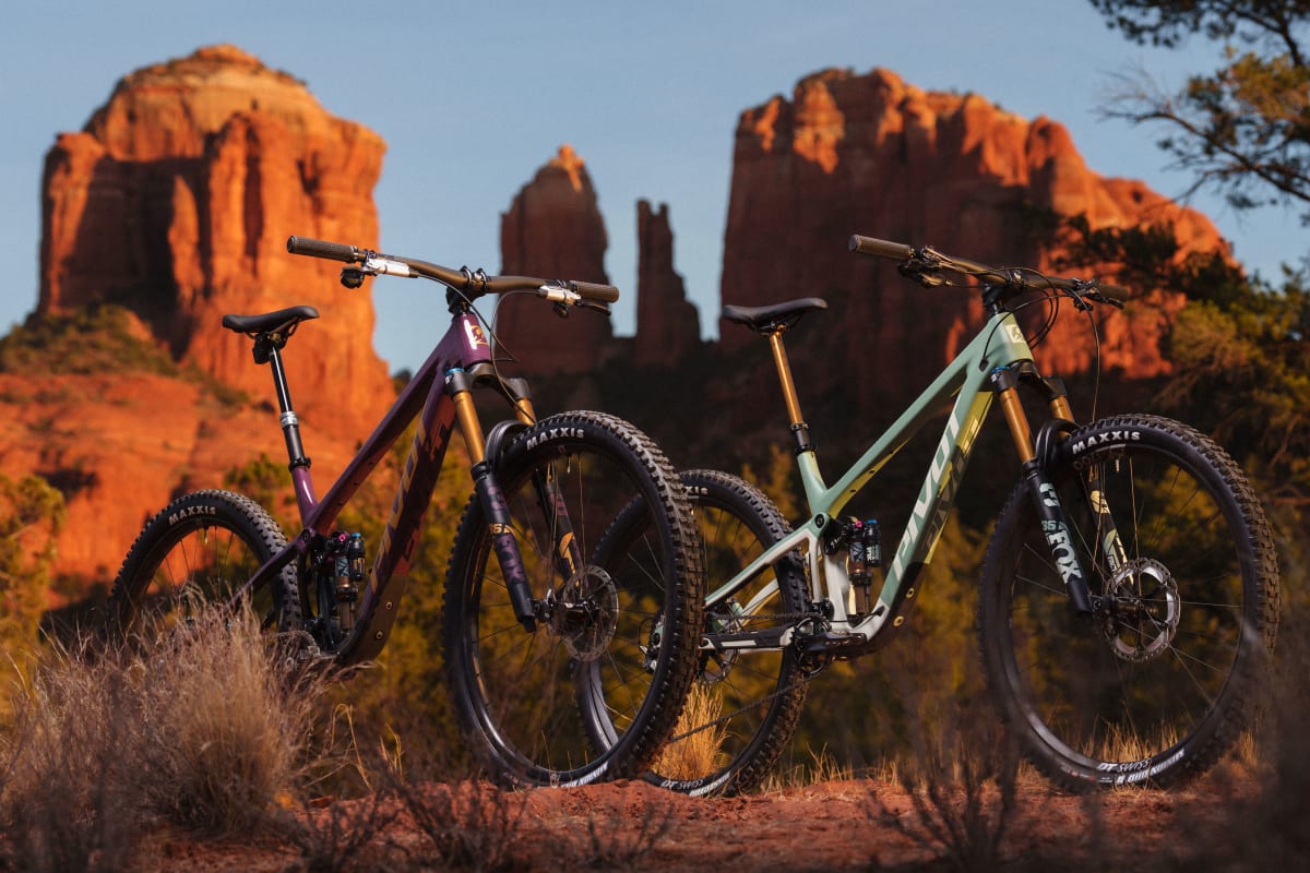 Two mountain bikes are parked on a dirt trail with red rock formations and desert vegetation in the background at sunset.