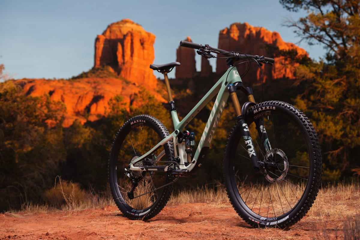 Pivot Trailcat LT full suspension mountain bike angled drive side view standing on a grassy field with the Sedona red rocks towering in the background