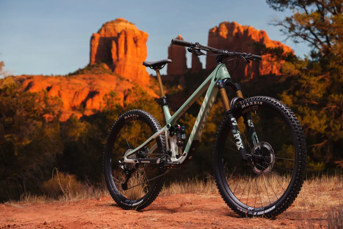 Pivot Trailcat LT full suspension mountain bike angled drive side view standing on a grassy field with the Sedona red rocks towering in the background