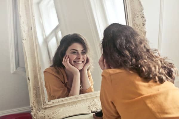 A smiling person looks at herself in the mirror