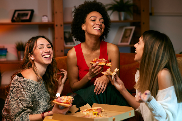 a group of three women eating pizza at home