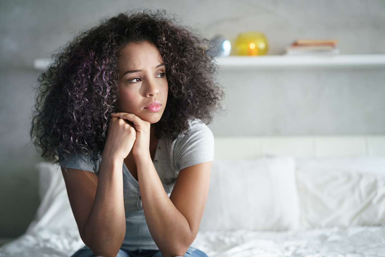 black woman sitting in bed with a worried expression on her face