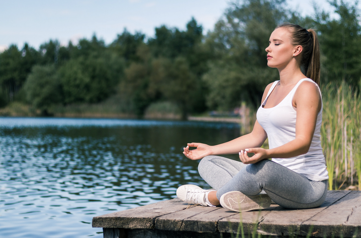 woman in lotus position meditating by the water