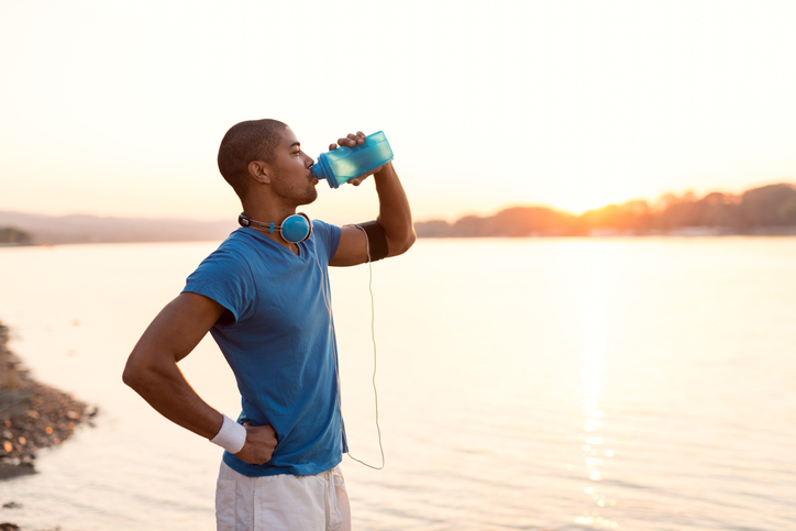 male jogger hydrating and resting by the lake