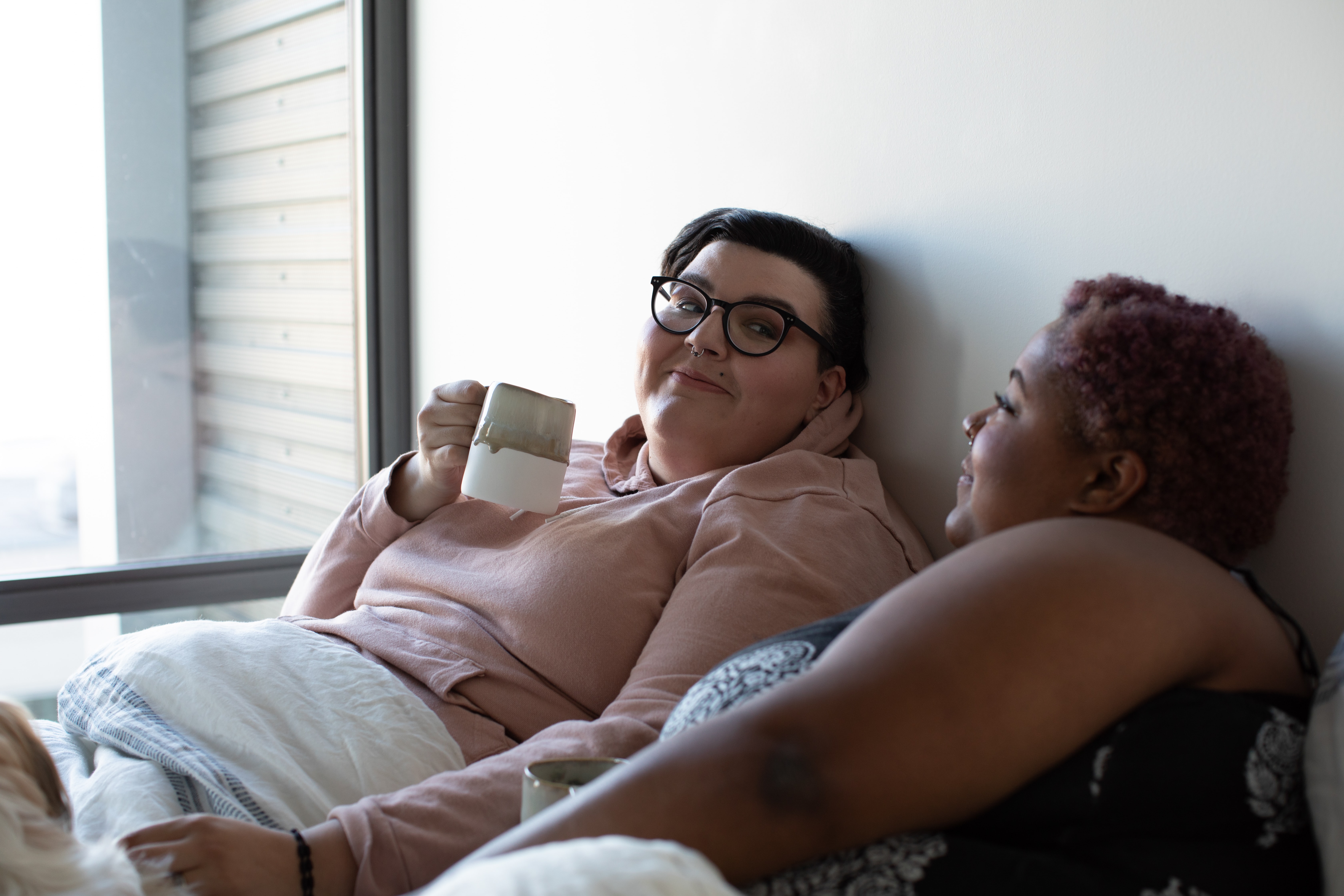 lesbian couple drinking coffee in bed