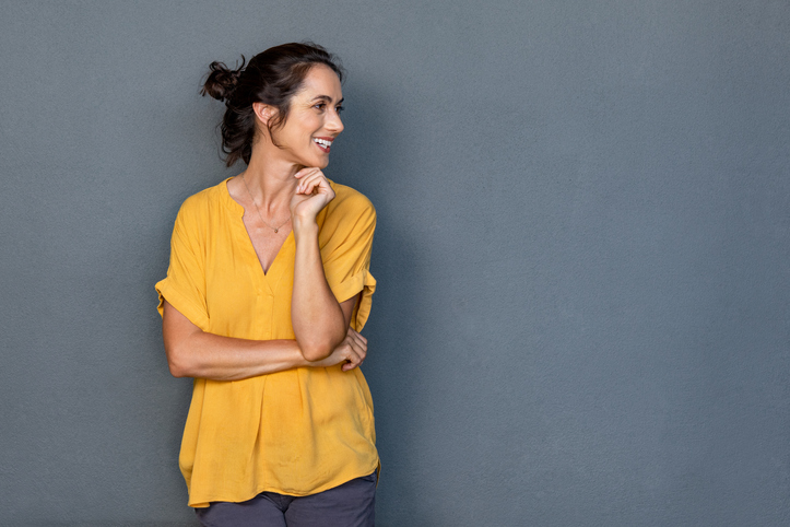 woman in yellow standing against a grey wall