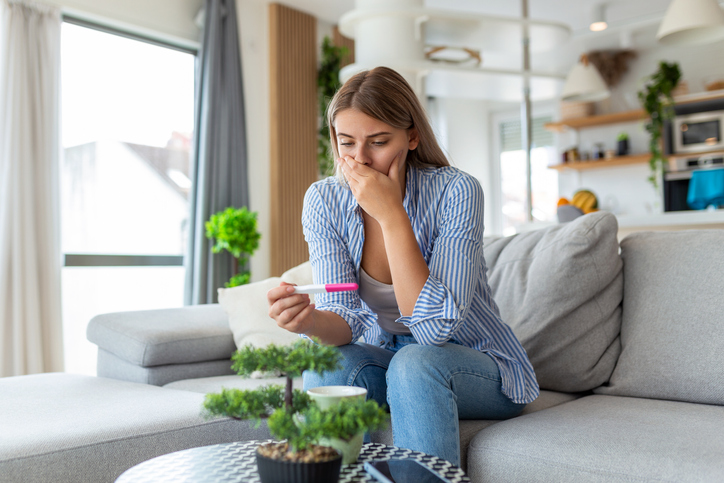 woman in shock staring at a pregnancy test