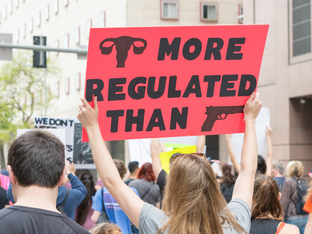 reproductive rights activist holding sign that reads "uteruses are more regulated than guns"