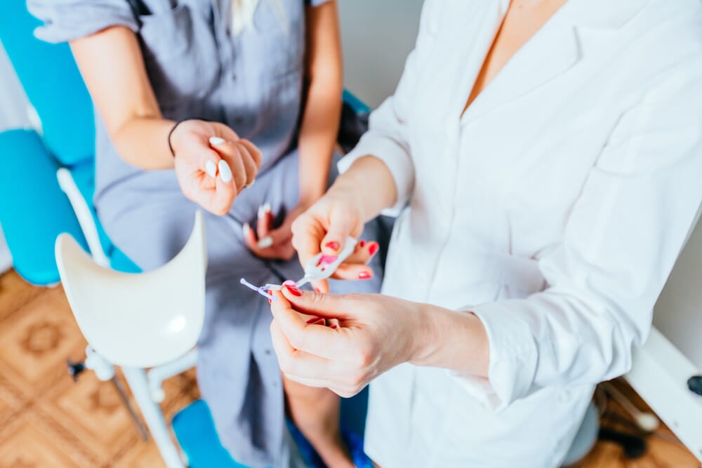 doctor holding a intrauterine device with patient on a bed