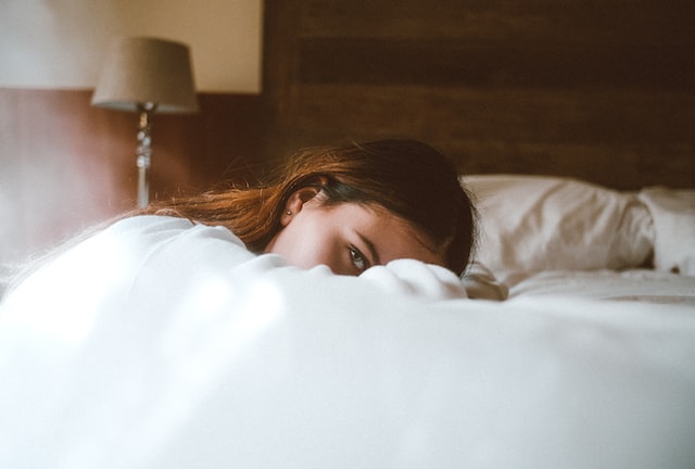 woman on a bed peeking out behind her folded arms