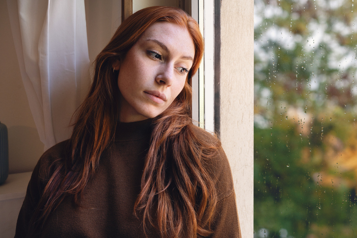 woman in distress staring out a window at the rainy weather