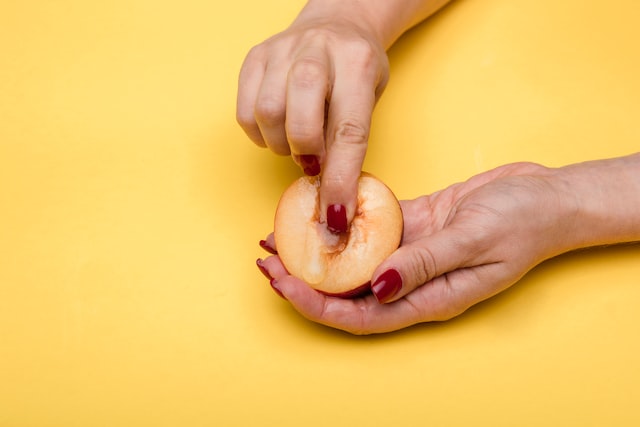 woman pressing her finger into the hollowed out core of a peach