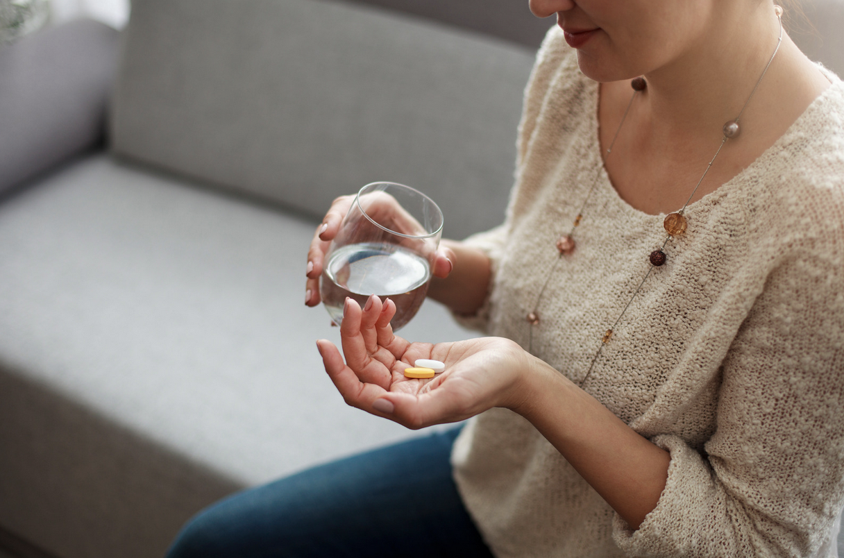 woman with a glass of water and a handful of fertility supplements