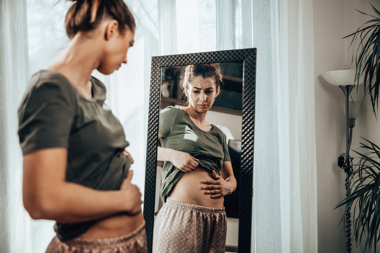 woman examining her endo belly in the mirror