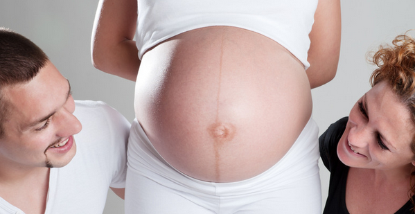 couple looking at their surrogate's growing belly