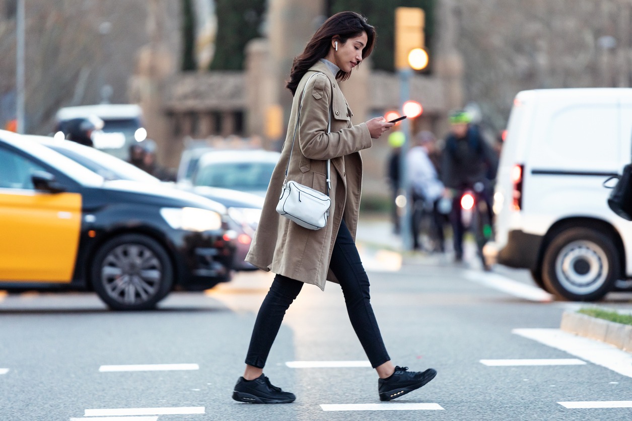 woman using her phone while walking in a city