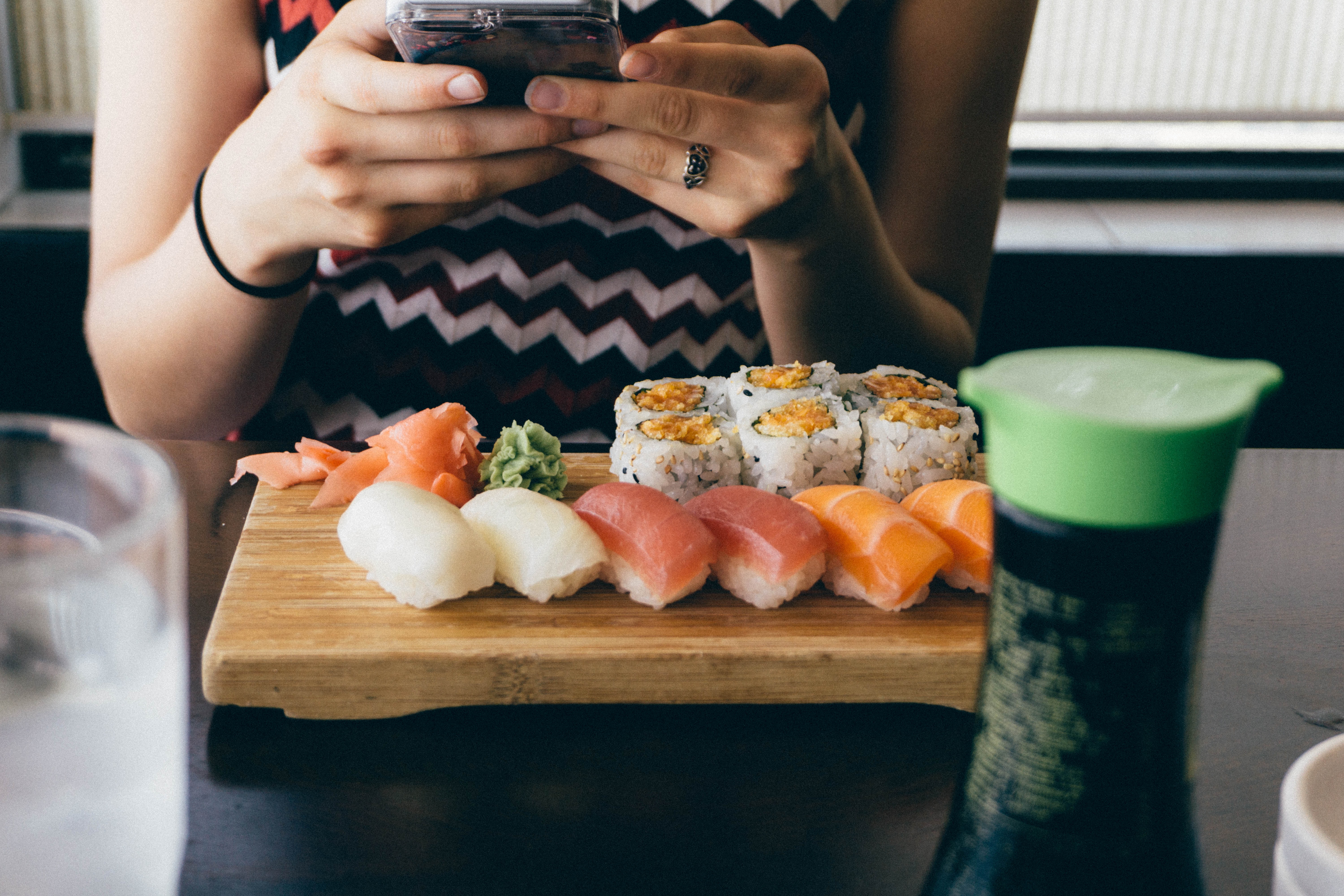 woman texting with a platter of sushi in front of her