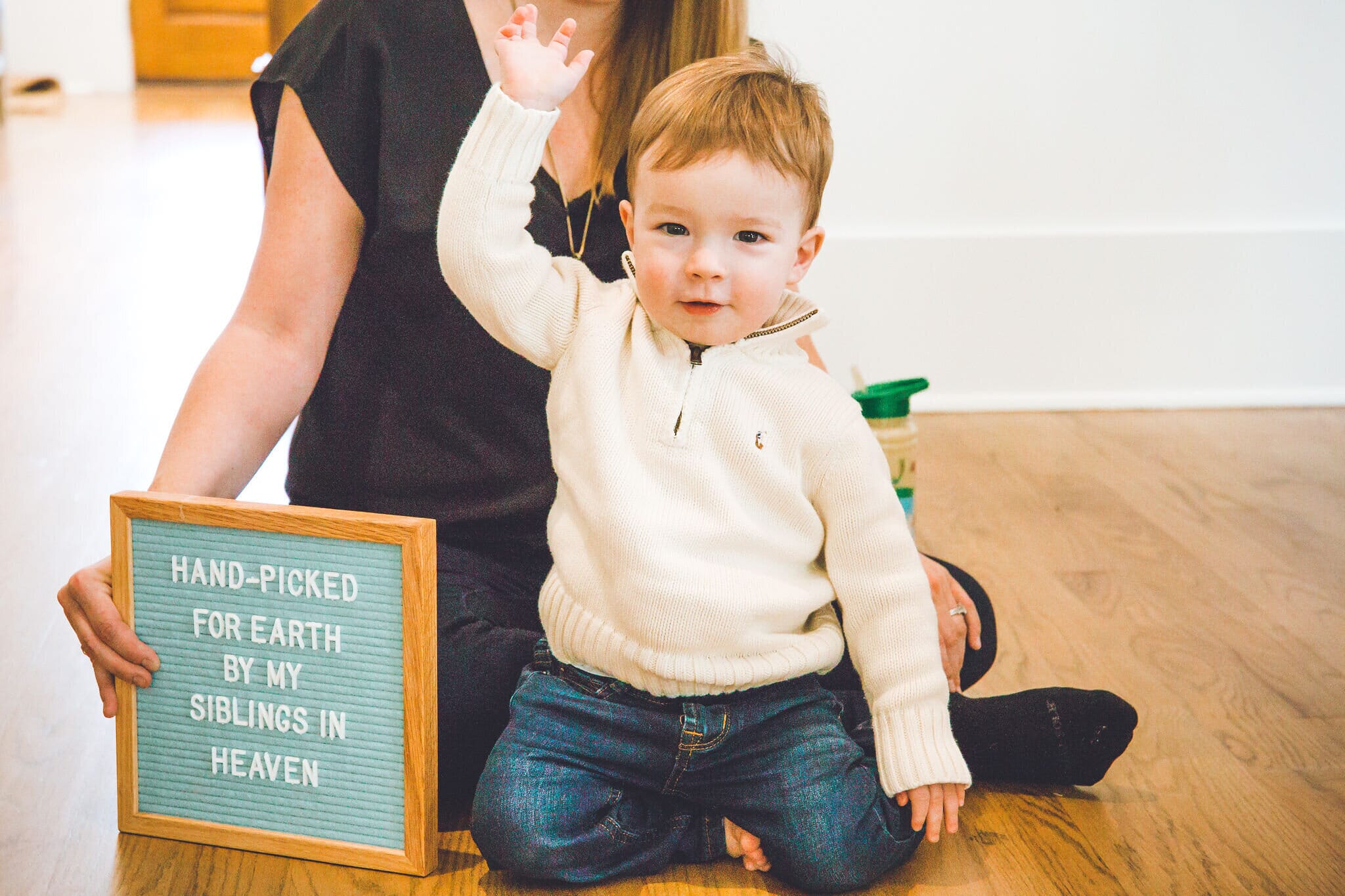 toddler sitting next to mother who is holding a sign that reads &quot;hand-picked for earth by my siblings in heaven&quot;