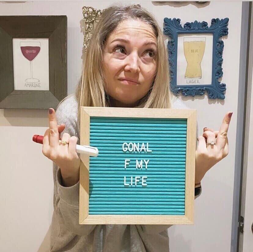 alexandra slate holding a sign that reads "gonal f my life" while flipping off the camera