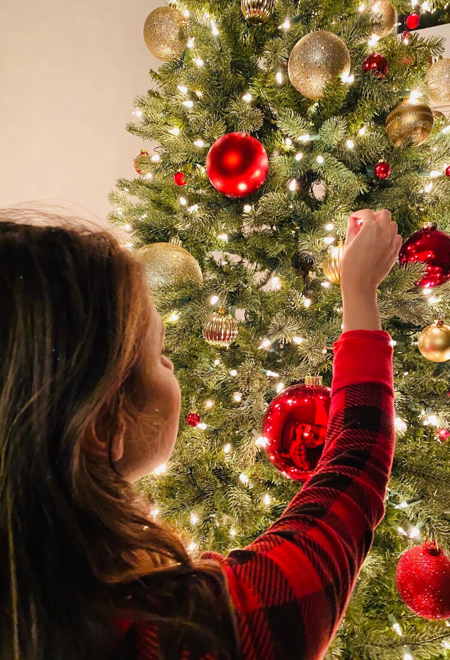 person putting ornaments on a christmas tree