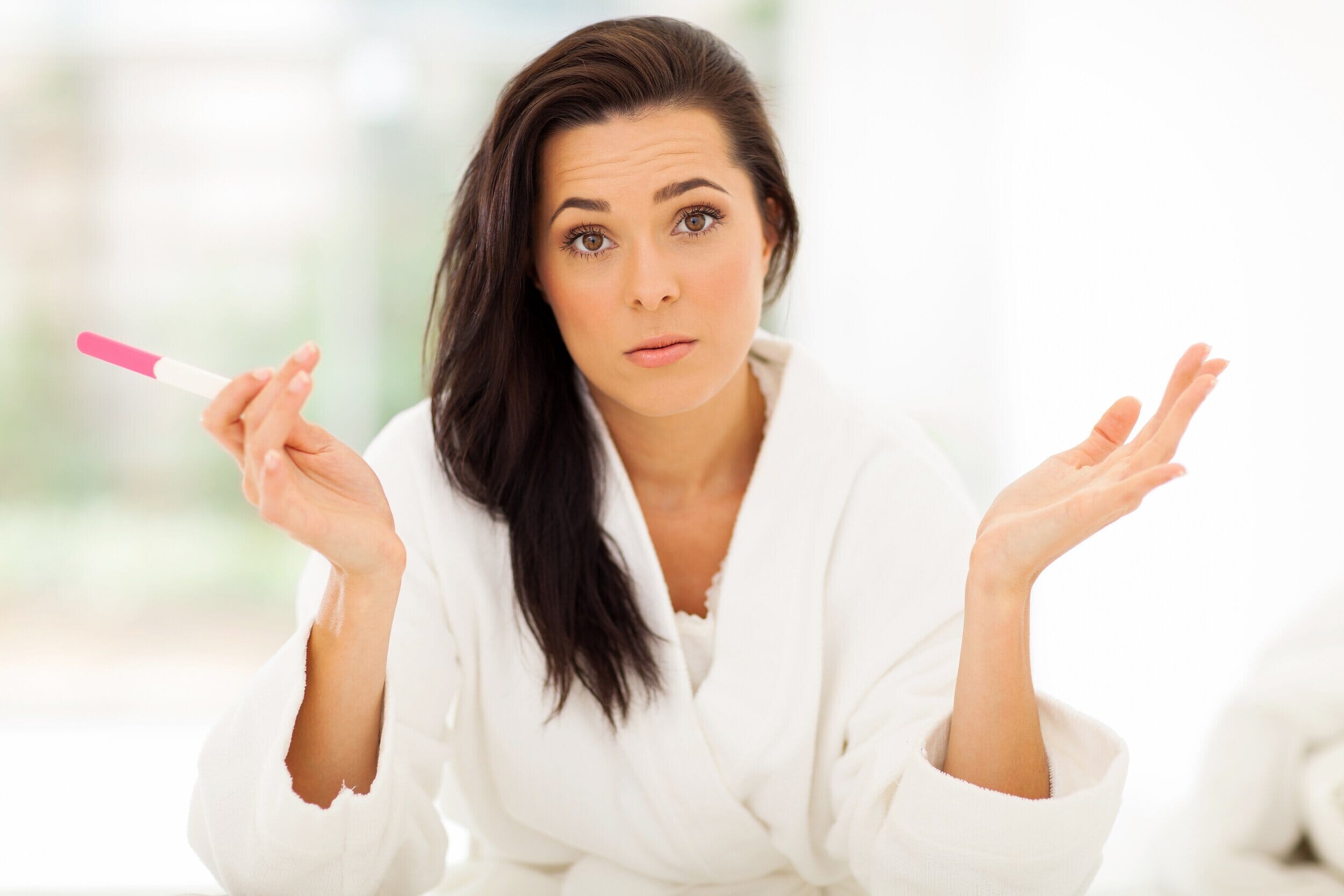 woman holding a pregnancy test with her hands up in the air in confusion