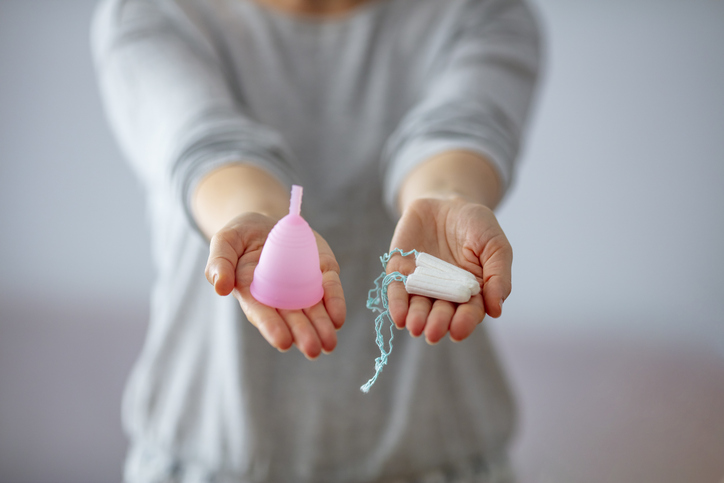 woman holding up one menstrual cup vs two tampons