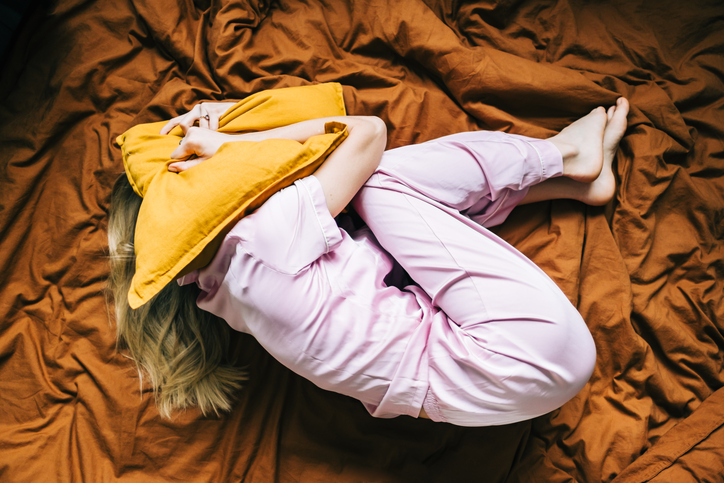 woman in fetal position head buried under a pillow
