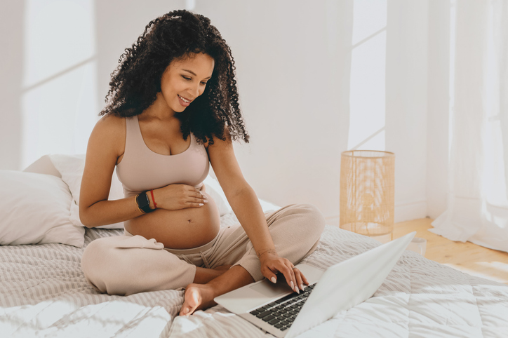 pregnant woman using a laptop in bed