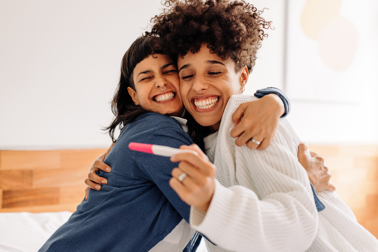 two women hugging and celebrating a positive pregnancy test