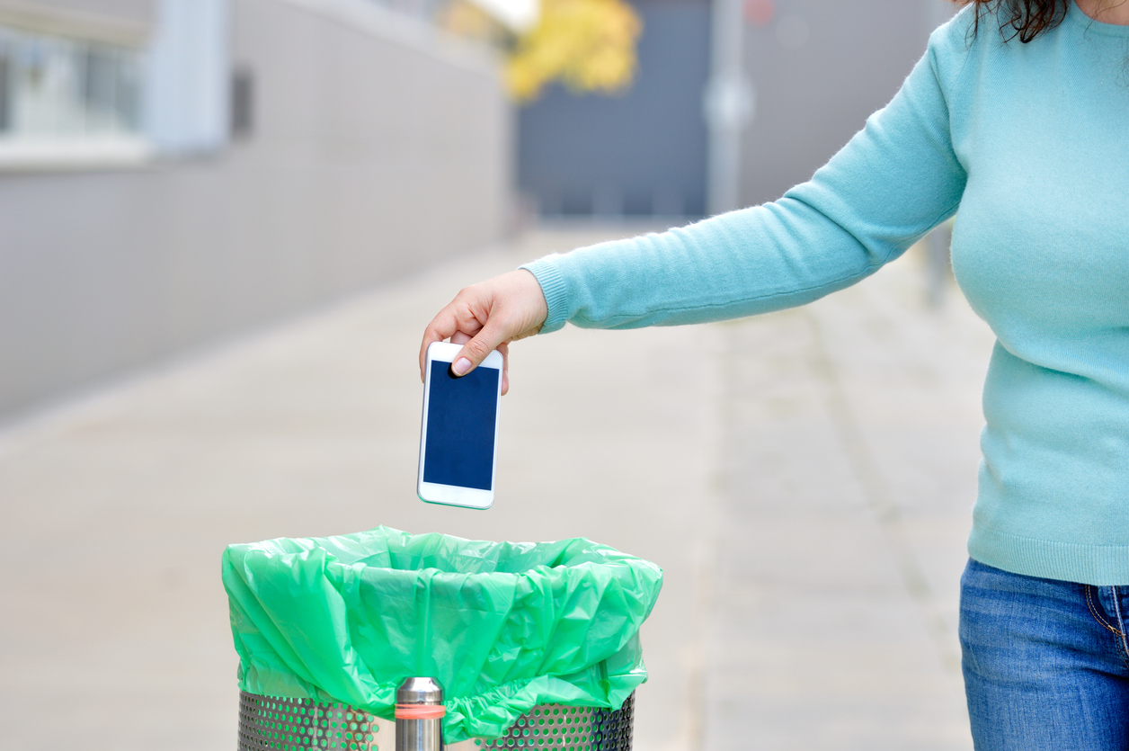woman holding her phone over a trash can