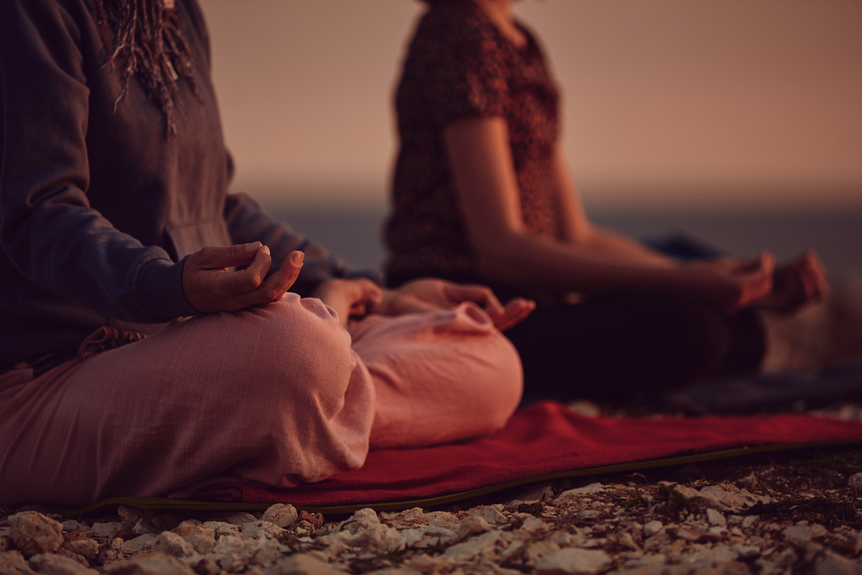 two women meditating side by side at sunset