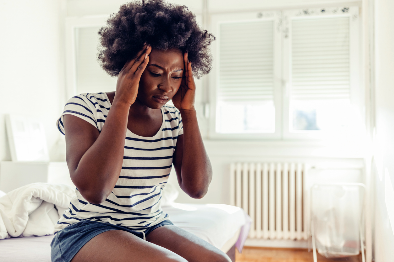 woman on the edge of her bed feeling a hormonal migraine coming on