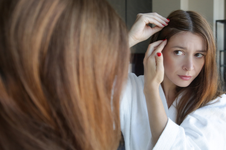 woman examining her gray hairs in a mirror