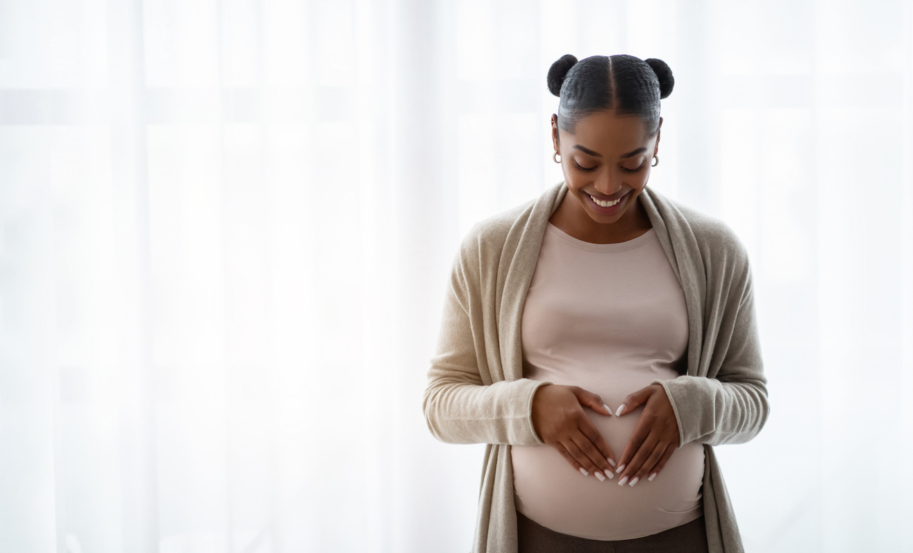 woman making a heart symbol over her pregnant belly