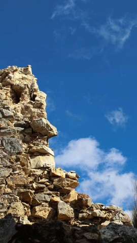 Partially destroyed rock wall with blue sky and white clouds in the background