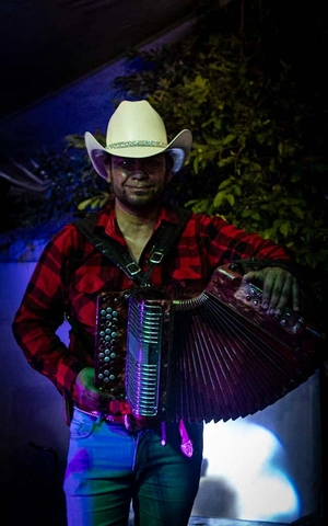 Man in a cowboy hat and a plaid shirt holding an accordion.