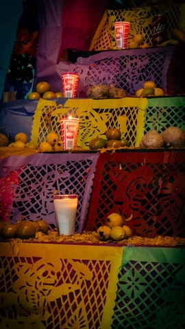 multi-tiered altar with papel picado, candles, fruits, and other objects