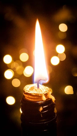 Зажженная свеча на темном основании с каплями воска и размытыми огнями на заднем плане