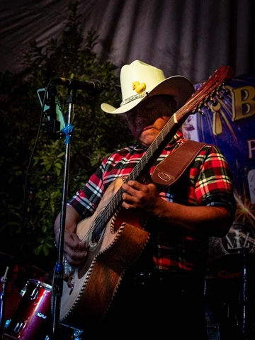 Homem com chapéu de caubói toca instrumento de cordas de doze cordas.