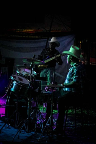 Dos hombres con sombrero de vaquero tocan instrumentos musicales en un escenario iluminado.